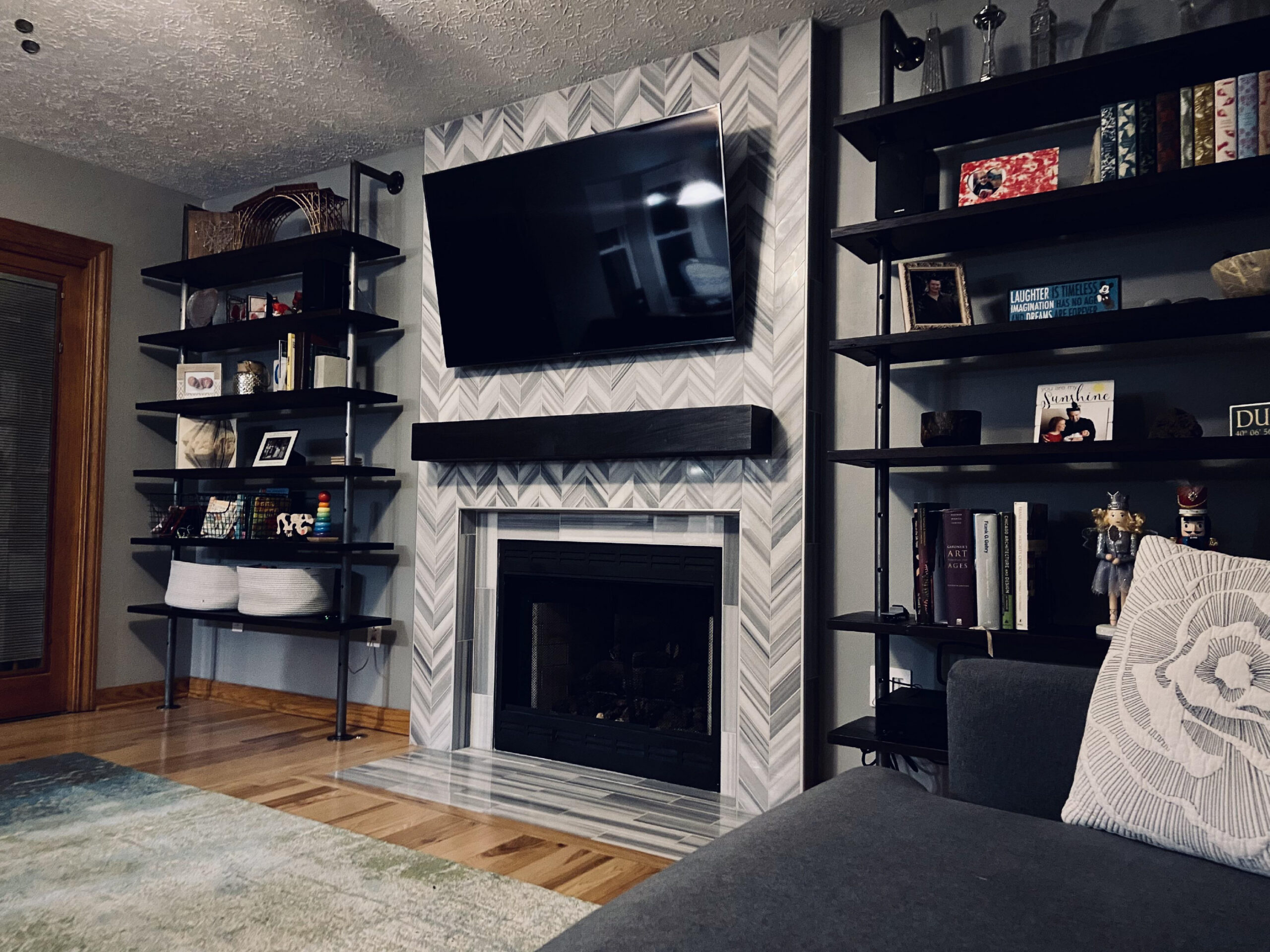 Living room with a fireplace, a couch with pillows, a carpet on the floor, bookshelves with books, photo frames, toys