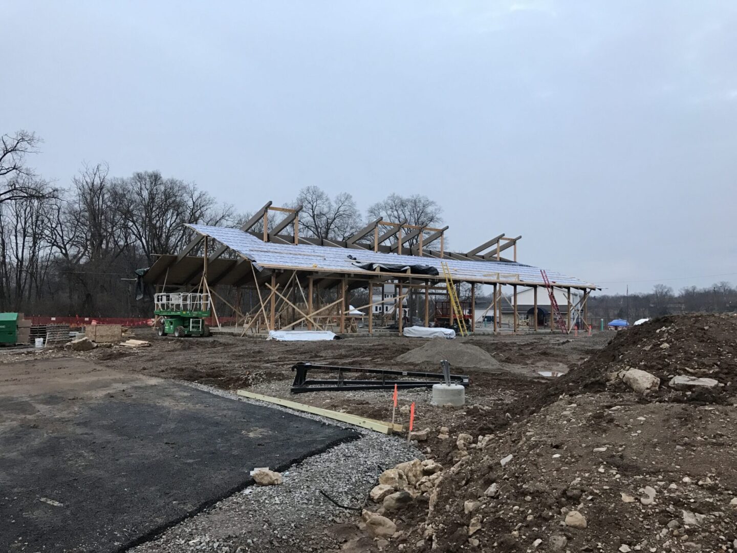 Large building under construction in the middle of a dirt field, surrounded by trees, poles, and other objects