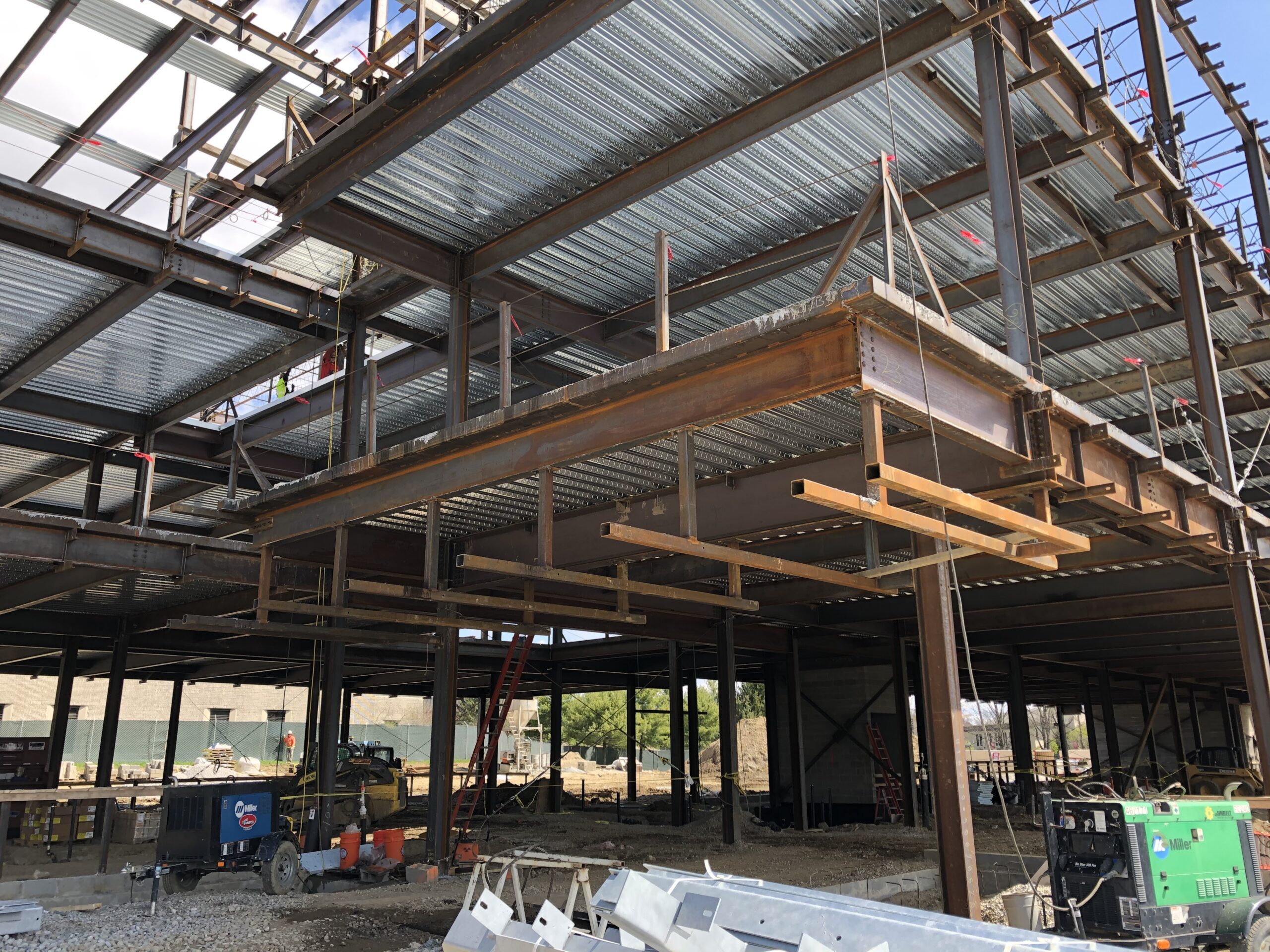 Large building under construction with a lot of metal beams, vehicles, and other objects on the ground