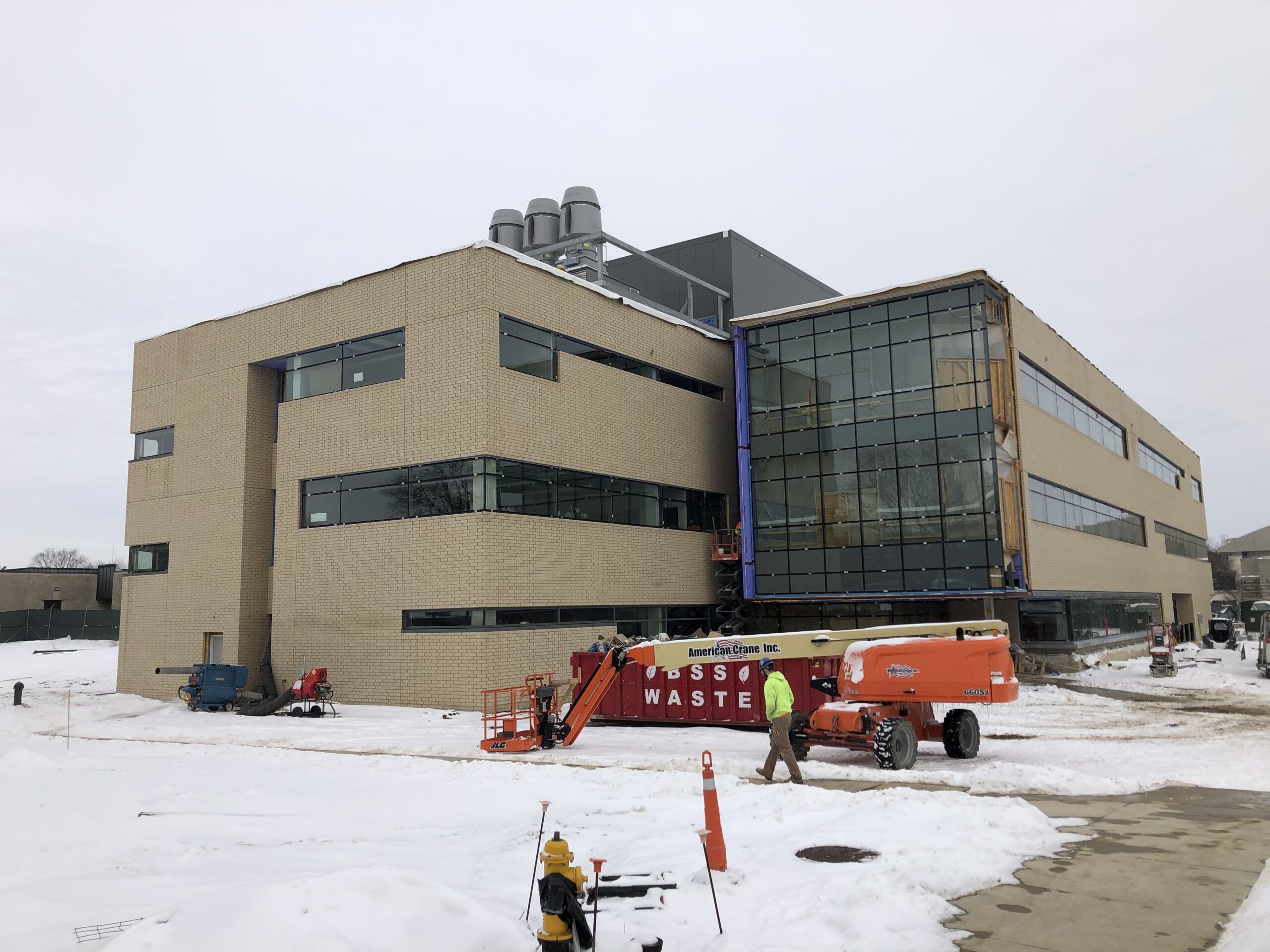 Large building with a crane in front of it, surrounded by vehicles, traffic cones, and other objects covered in snow