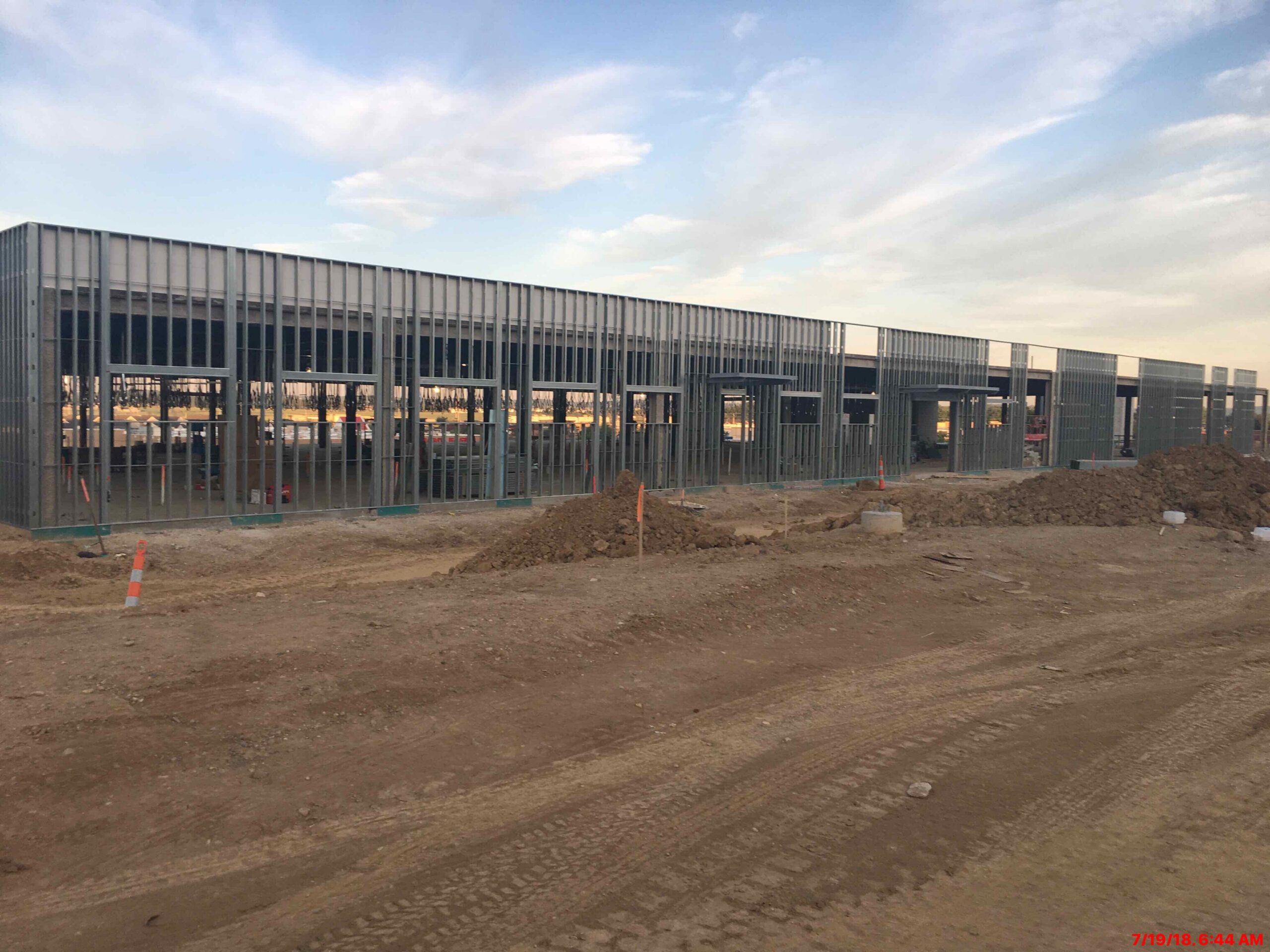 Large building under construction in the middle of a dirt field, surrounded by poles, traffic cones, and other objects