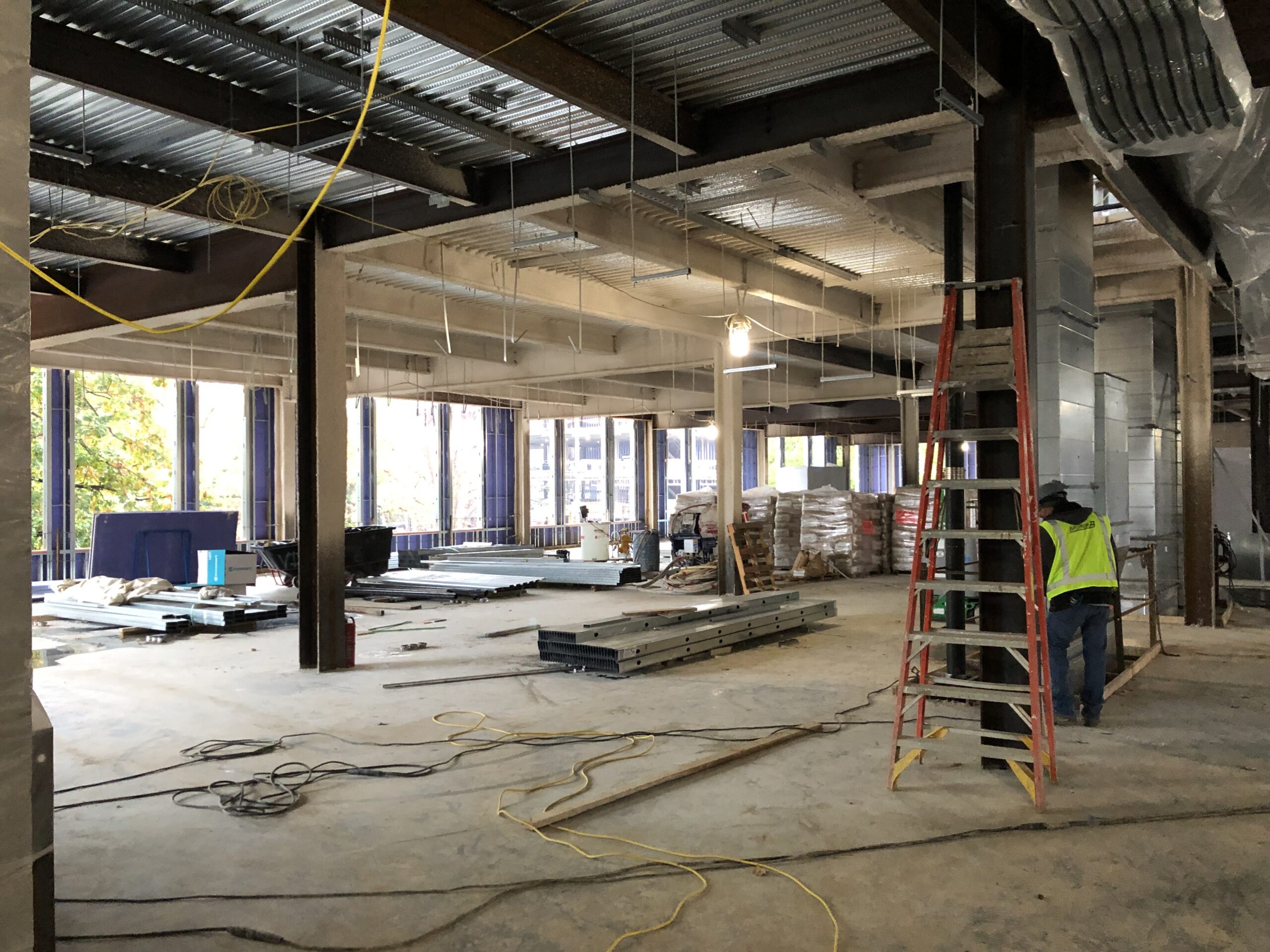 Man standing on a ladder in a large room with a lot of construction equipment, including wires, wooden objects, pillars