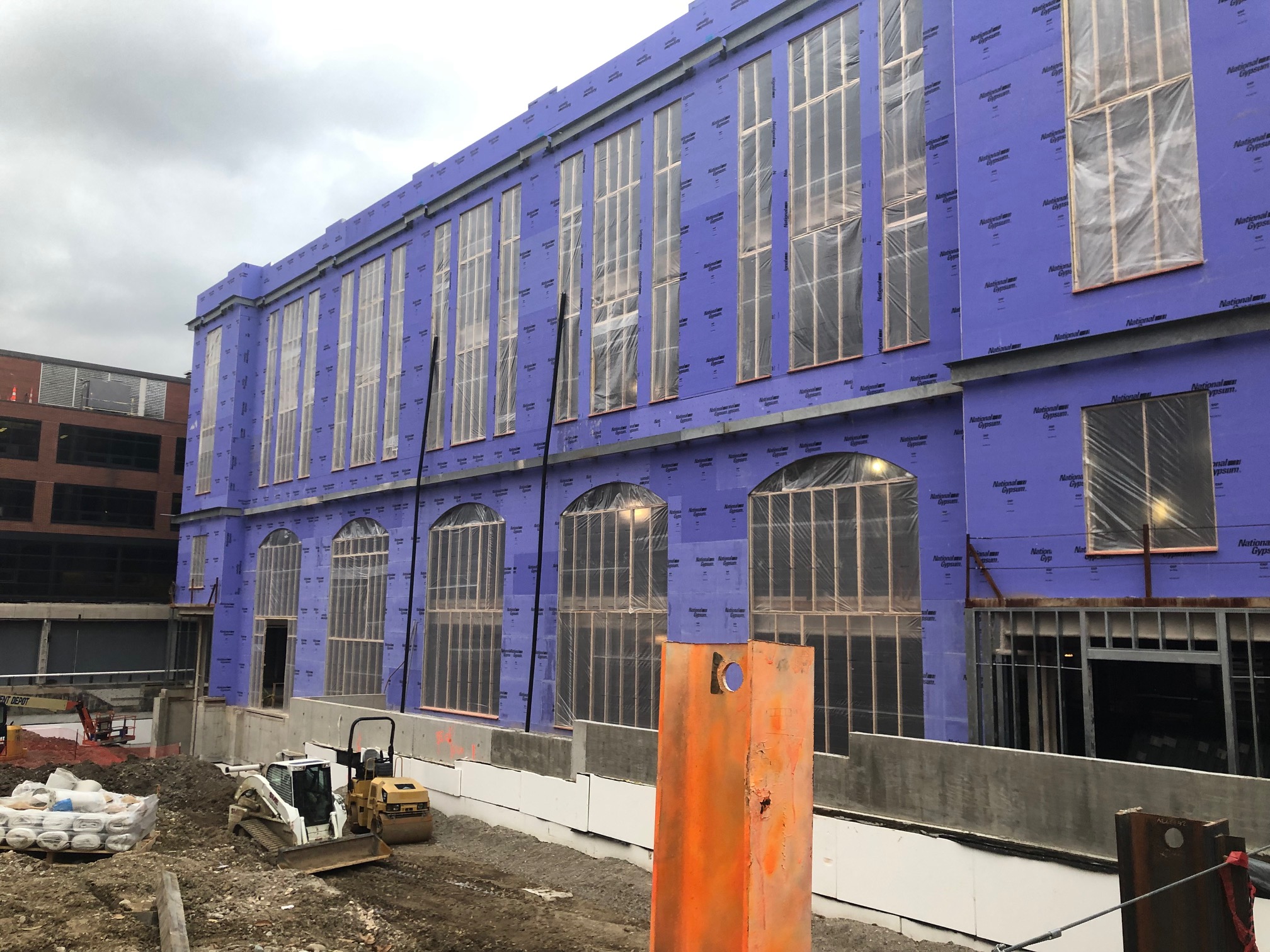 Large building under construction with a lot of windows, surrounded by vehicles, sandbags, and other objects on the ground