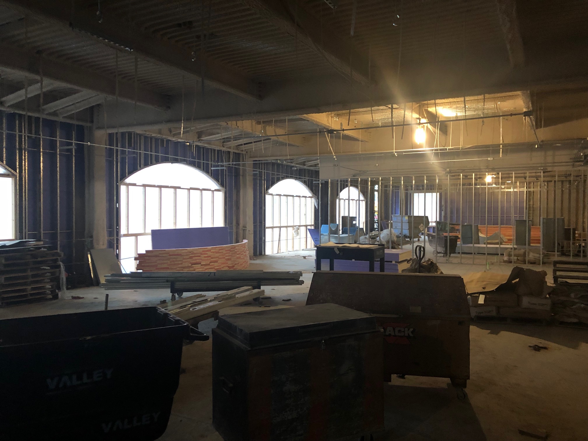 Large room filled with lots of furniture and windows, including tables, wooden objects, and other objects on the floor